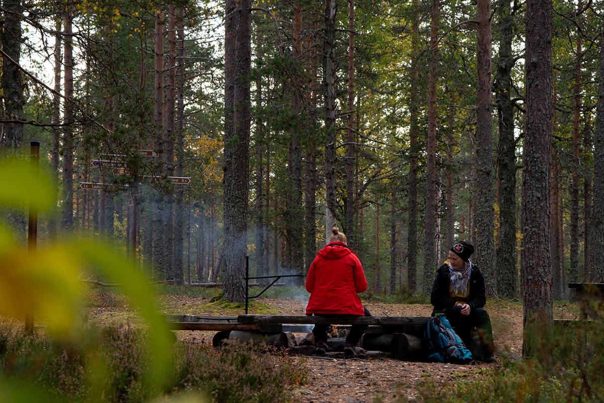 Kaksi ihmistä istuvat nuotiopaikalla Spitaalijärvellä.