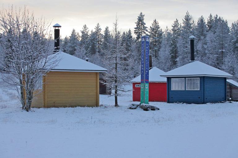 Parran talvipuistossa voit valita neljän eri tulipaikan välillä. Kuvassa keltainen, sininen, punainen ja puun värinen grillikatos sekä Talvipuiston kyltti. Talvinen luminen maisema.