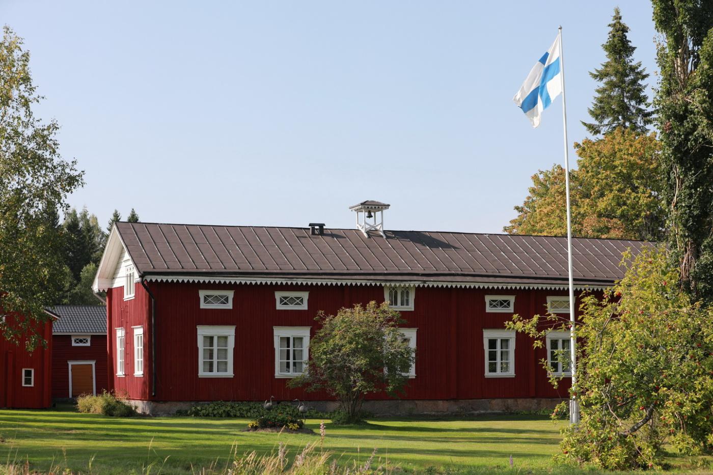 Punainen maalaistalo, etualalla lippusalko, jossa Suomen lippu.