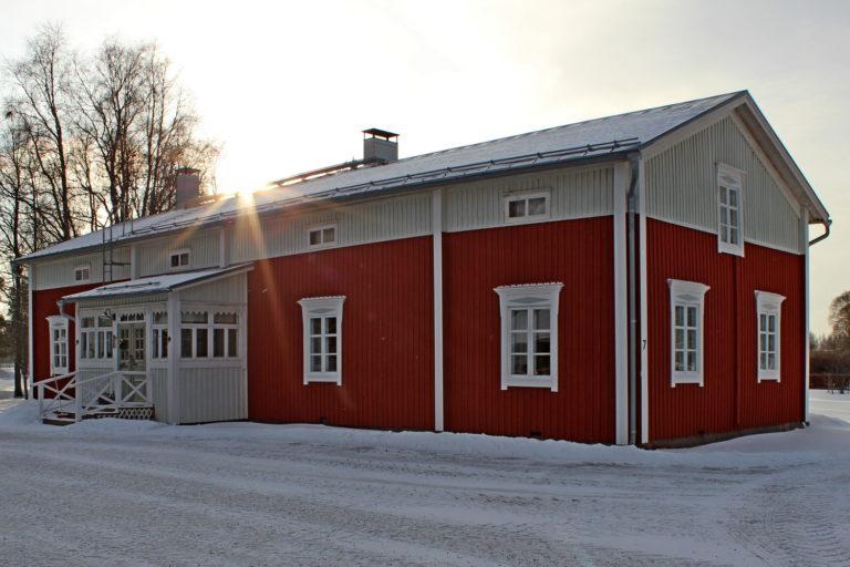 Talvinen kuva punavalkoisesta puurakennuksesta, kuvattu etuviistoon.