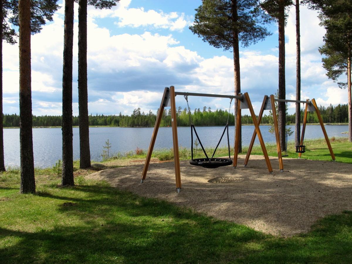 Kesäisessä kuvassa etualalla lasten hämähäkkikeinu, taustalla siintää Säläisjärvi.