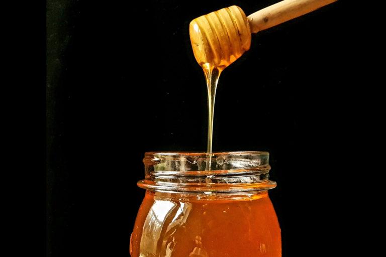Hunajapurkki ja hunajatikku josta valuu juoksevaa hunajaa.